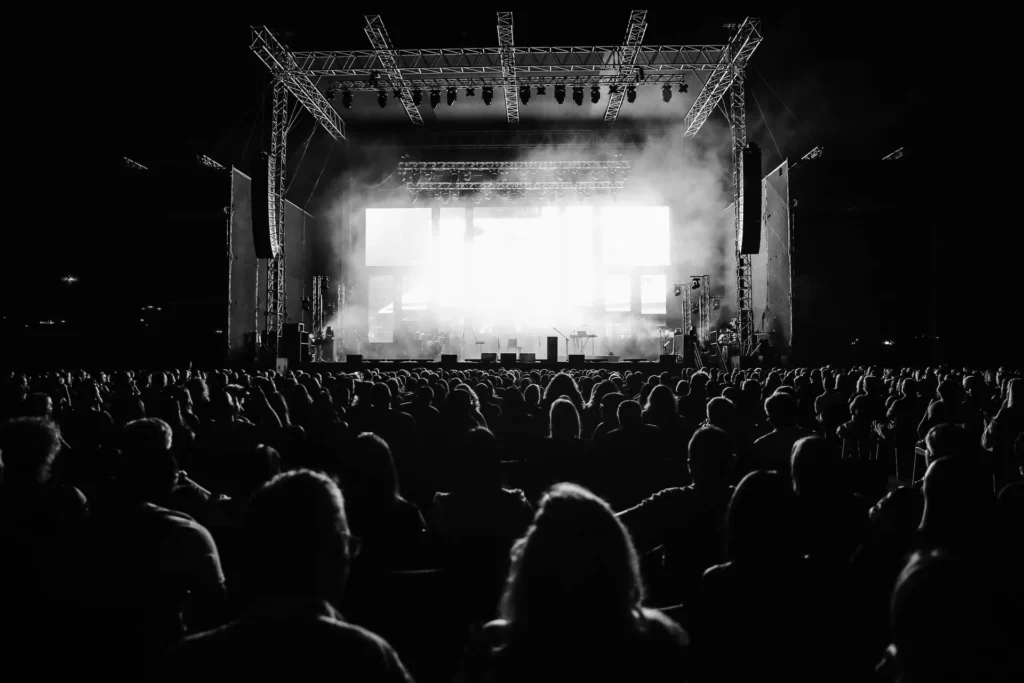 Concert audience facing a lit outdoor stage at night
