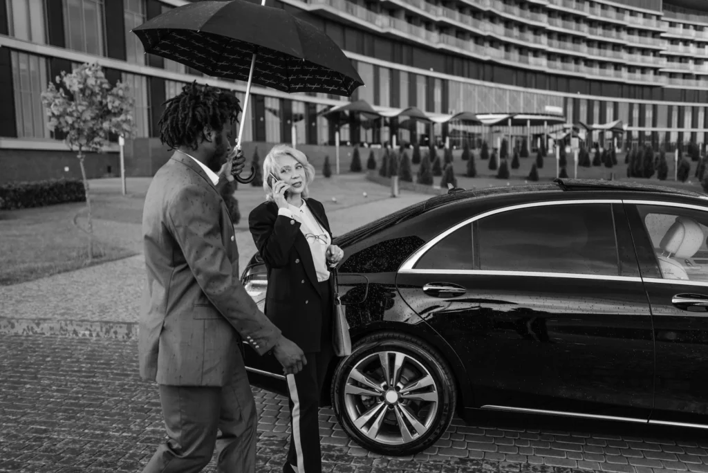 Close protection agent holding an umbrella for a client beside a waiting car